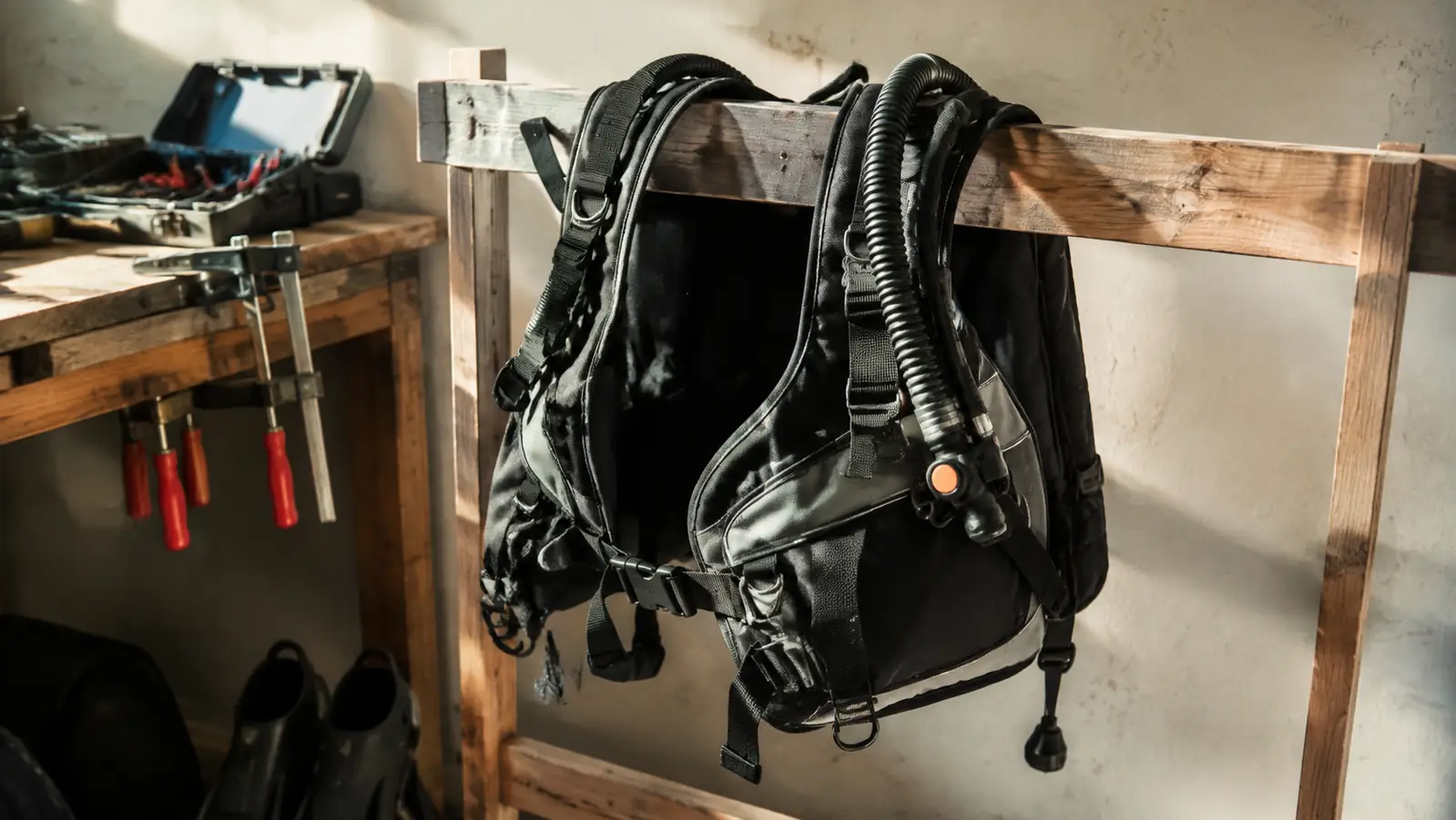 A back-inflation BCD hanging flat to dry in a rustic gear room beside a wooden workbench and clamps