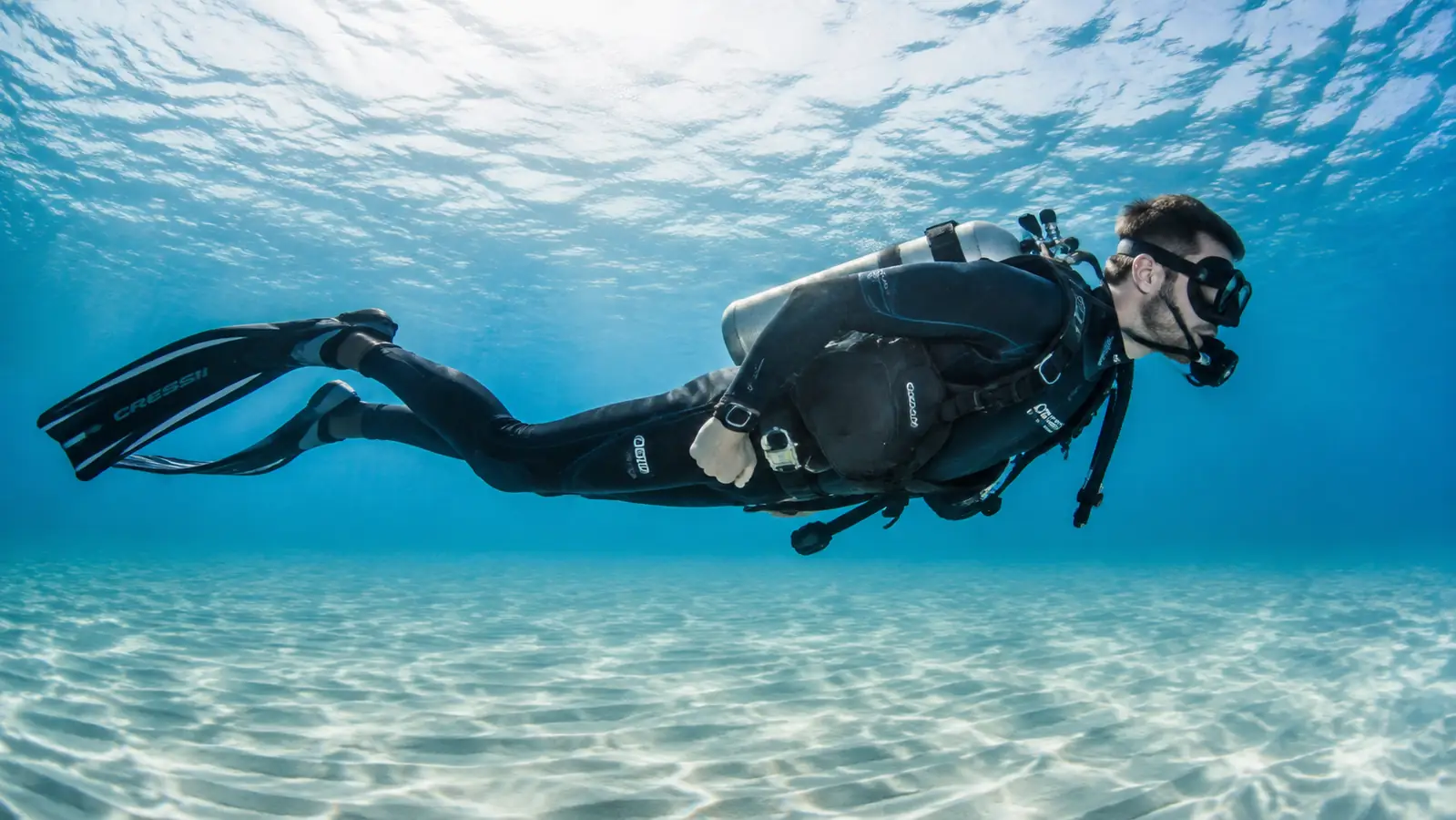 Diver floating flat and horizontal near the surface, finning slowly with wide calm kicks, one hand resting near the weight belt